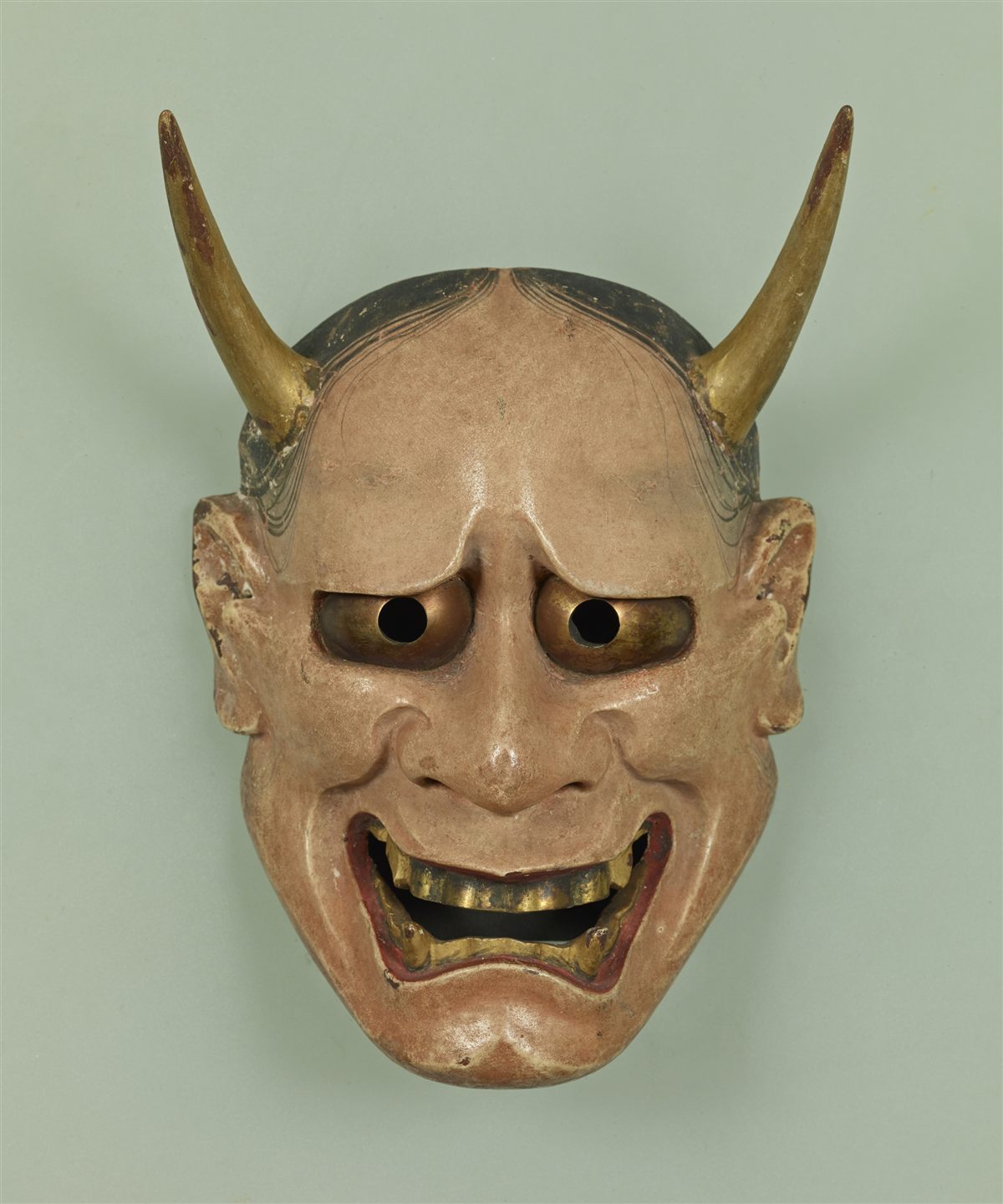 Traditional Japanese Hannya Noh mask with gold horns, fangs, and a pale lacquered face