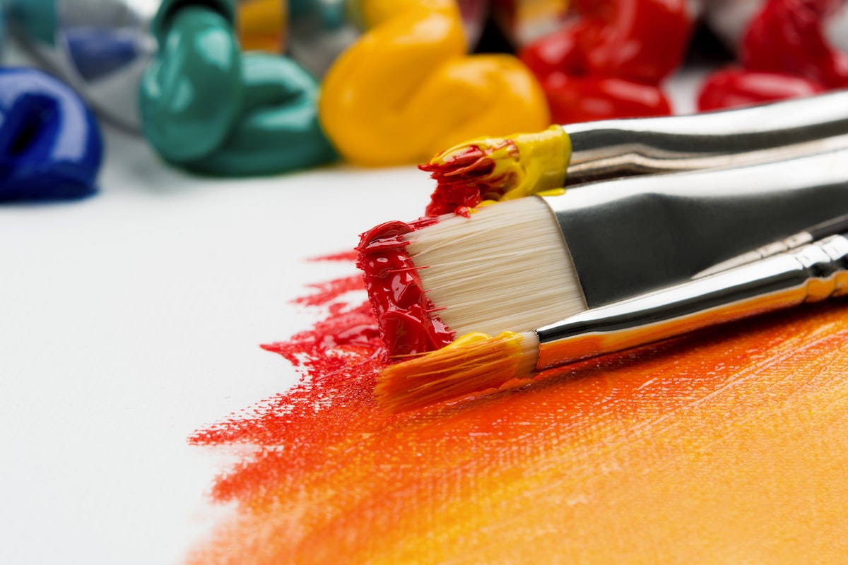 Close-up of brushes loaded with deep red and gold pigment on a studio surface